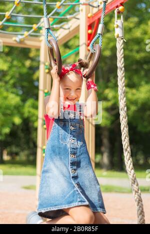 ittle girl playing on the playground. the child hung on the gymnastic rings swing Stock Photo