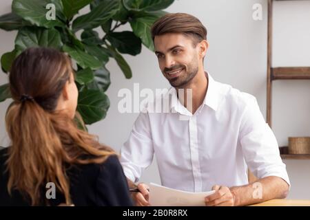 Smiling hr manager holding resume in hands, talking with candidate on job interview in office, good first impression, hiring process, friendly employe Stock Photo