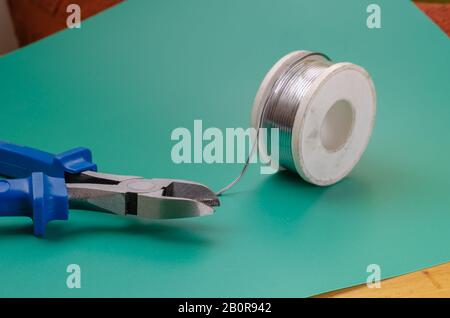 Side view of wire cutters with blue handles and a dirty coil of solder. DIY or industry. Close-up. Selective focus. Eye level shooting. Stock Photo