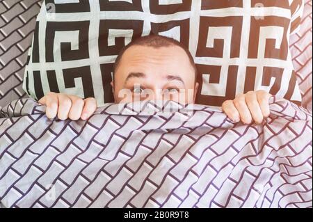 The frightened man in the bed hid under the blanket Stock Photo