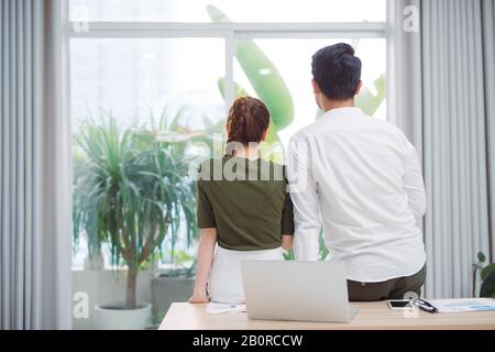 Cute couple looking out the window after work Stock Photo