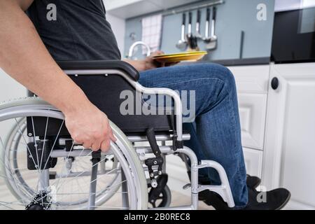 Handicapped Man Sitting On Wheelchair In Kitchen Holding Dishes Stock Photo