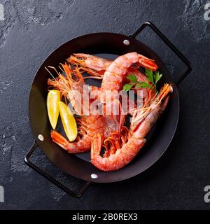 Prawns with lemon and fresh herbs in a black frying pan. Stone background. Top view. Stock Photo