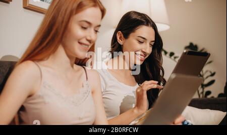 Two beautiful caucasian ladies are using their gadgets while smiling cheerfully and relaxing from work days