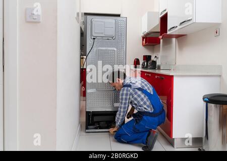 Young Male Serviceman Repairing Broken Refrigerator In Kitchen Stock Photo