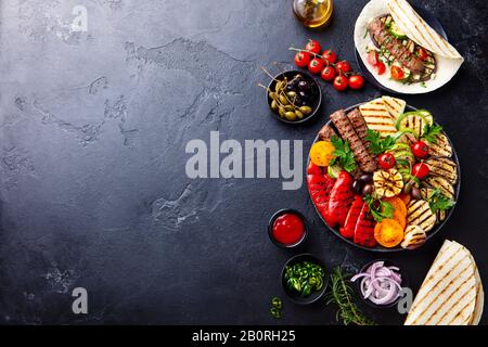 Meat kebab, vegetables on a black plate with tortillas, flat bread. Slate stone background. Copy space. Top view. Stock Photo