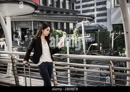 Beautiful young businesswoman walking outside public transportation station. Businesswoman traveler with suitcase on the way to the airport. Stock Photo