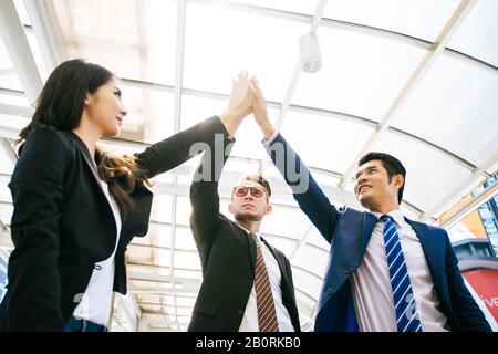 Successful business team is giving high five and smiling while standing in front of office. Stock Photo