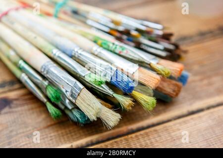 A closeup of the few paintbrushes with traces of paint on them on the wooden table