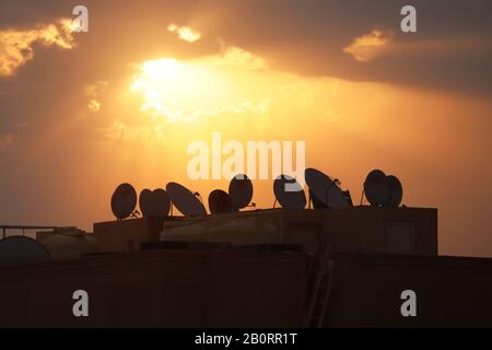 Satellite television dishes clustered on rooftop with rising sun Stock Photo