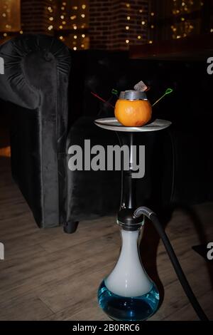 Oriental hookah with orange stands on the floor against the background of lighting in a cafe. Dark night is a magical scene. Stock Photo