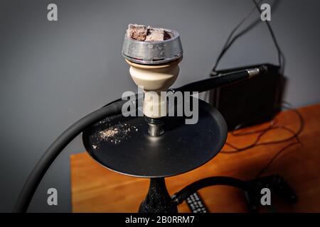 Black matte hookah with clear water with a black hose on the table next to the remote control in the lounge bar on a light background. Hookah cafe lei Stock Photo
