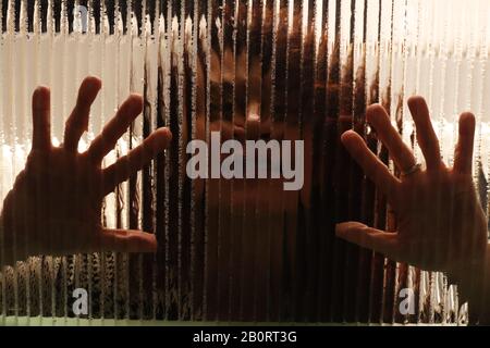 Creepy scary image of girl behind glass with palms of hands on textured glass Stock Photo