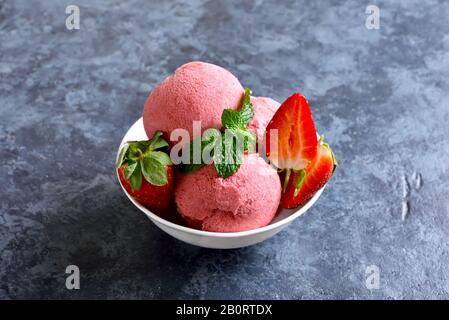 Strawberry ice cream scoops with fresh strawberries in bowl over blue stone background. Tasty summer cold dessert. Close up view Stock Photo