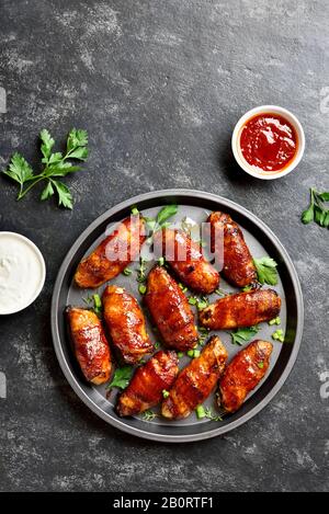 Tasty bacon wrapped grilled chicken wings on plate over dark stone background with free space. Tasty snack from chicken meat, bacon in sweet, sour, sa Stock Photo