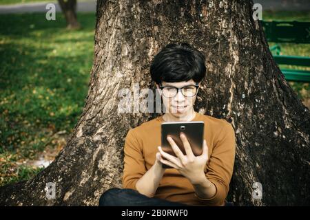 young man using a tablet and sitting under the tree Stock Photo