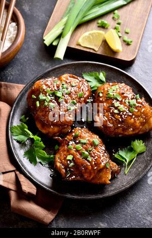 Sweet and spicy honey grilled chicken thighs on plate over dark stone background. Tasty food in asian style. Stock Photo