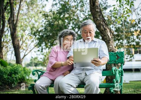 Cheerful senior woman and man using digital tablet on bench at the park Stock Photo