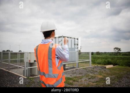 Asian engineer with hardhat using  tablet pc computer inspecting and working at wind turbine farm Power Generator Station Stock Photo