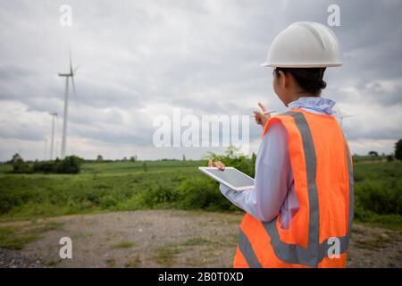 Asian engineer with hardhat using  tablet pc computer inspecting and working at wind turbine farm Power Generator Station Stock Photo