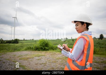Asian engineer with hardhat using  tablet pc computer inspecting and working at wind turbine farm Power Generator Station Stock Photo