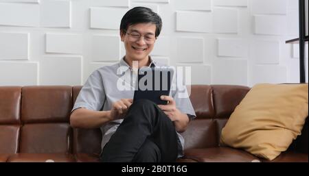 Senior Asian man playing tablet and video call on sofa in living room at home  Portrait of Asian elderly man is Relaxing and Happiness With playing ta Stock Photo