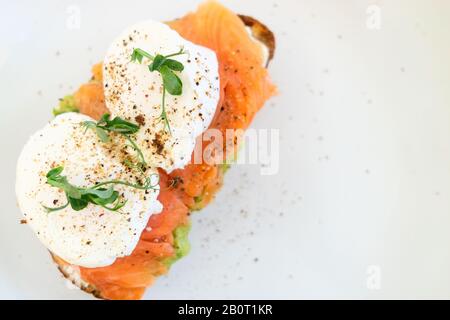 Healthy food. Sandwich with slightly salted salmon: grain bread, cream cheese, guacomolla cheese, fish, poached egg, avocado, greens over white background. Stock Photo