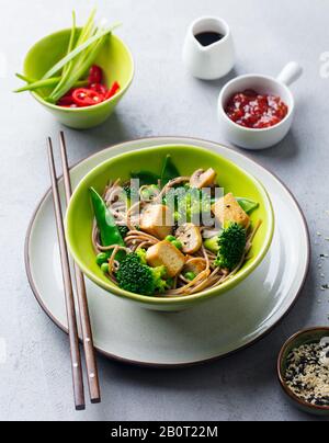 Soba noodles with vegetables and fried tofu in a bowl. Grey background. Stock Photo