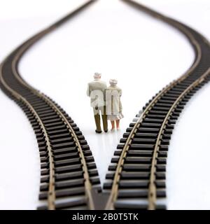 Couple of elderlies, two figurines between two tracks leading into different directions, symbolic image for making decisions Stock Photo
