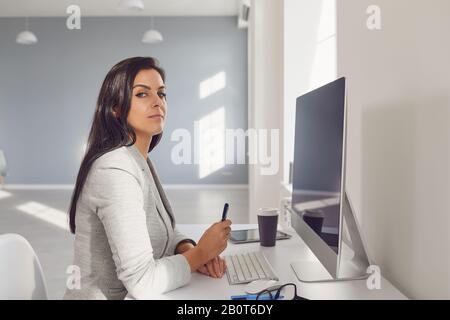 Serious businesswoman working sitting at a table with a computer in the office. Stock Photo