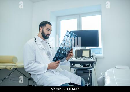 Male bearded doctor in a white robe analyzing MRI results looking thoughtful Stock Photo