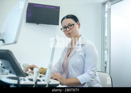 Female doctor in eyewear sitting at the ultrasonic device Stock Photo