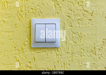 A white light switch on a yellow concrete wall.Turn the lights on or off. Stock Photo