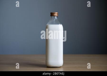 front view closeup of full closed one liter glass bottle of fresh milk on light colored wood table in natural lighting against a grey wall  background Stock Photo