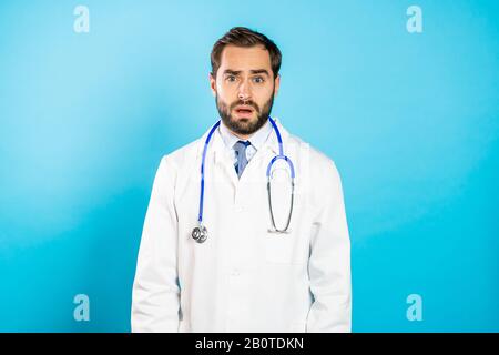 Portrait of young disappointed man in professional medical white coat on blue Stock Photo