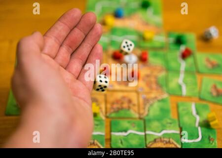Hand throws the dice on the background of colorful blurred fantasy Board games, gaming moments in dynamics. selected focus. Stock Photo