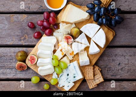 Cheese and Fruits Assortment on Cutting Board with Red, White Wine on  Wooden Background. Stock Photo by annapustynnikova