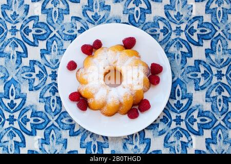 Lemon, vanilla bundt cake with raspberry on blue background. Top view. Close up. Stock Photo