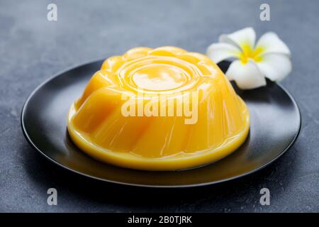 Mango pudding, jelly, dessert on black plate. Grey stone background. Close up. Stock Photo