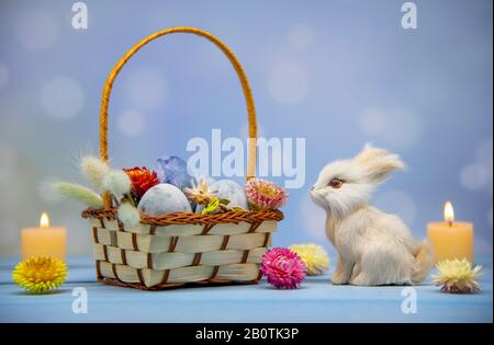 A basket full of Easter eggs painted blue, a hare and burning candles  Stock Photo