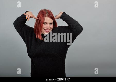 Young redhead fat lady in black sweater funny woman holds hands above head Stock Photo