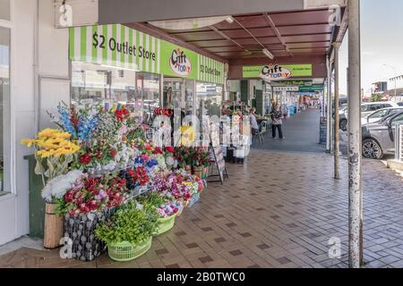 THAMES, NEW ZEALAND - November 07 2019: cityscape of historical village with fake flowers on sale under commercial buildings covered walkway on main s Stock Photo