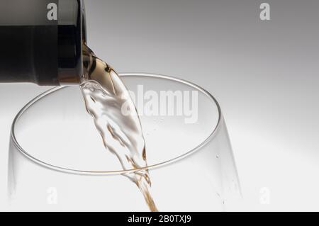 macro shot of pouring white wine from the bottle into a still empty glass Stock Photo