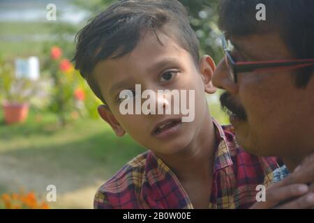 Close up of a squint eyed, strabismus, crossed eyed young boy on the lap of  a  man wearing spectacles, Stock Photo