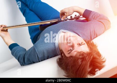Happy young man lying back on sofa with guitar Stock Photo