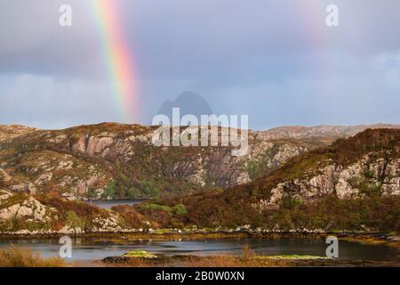 Rainbow in dark sky over Suilven mountain in remote Scottish Highlands landscape in Assynt North West Scotland Stock Photo