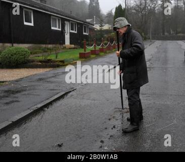 Kilbarchan, Scotland, UK. 21th February 2020.  Residents attempt to divert water flooding down their street by unblocking drains. Stock Photo