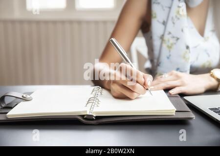 Closeup of woman's hand writing on notebook. Freelance journalist working at home. Stock Photo