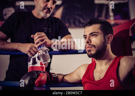 Portrait of boxing coach and male boxer sitting in boxing ring. Stock Photo