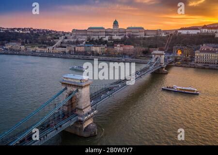 Budapest, Hungary - Aerial view of Szechanyi Chain Bridge and Buda Castle Royal Palace with a beautiful golden sunset and sightseeing boats on River D Stock Photo